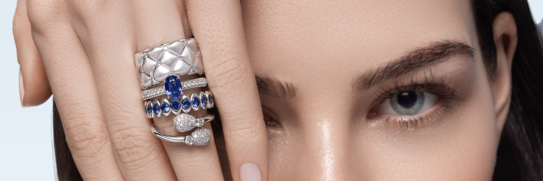 Close-up of a woman's face with a focus on her eye, wearing multiple Fabergé rings on her fingers