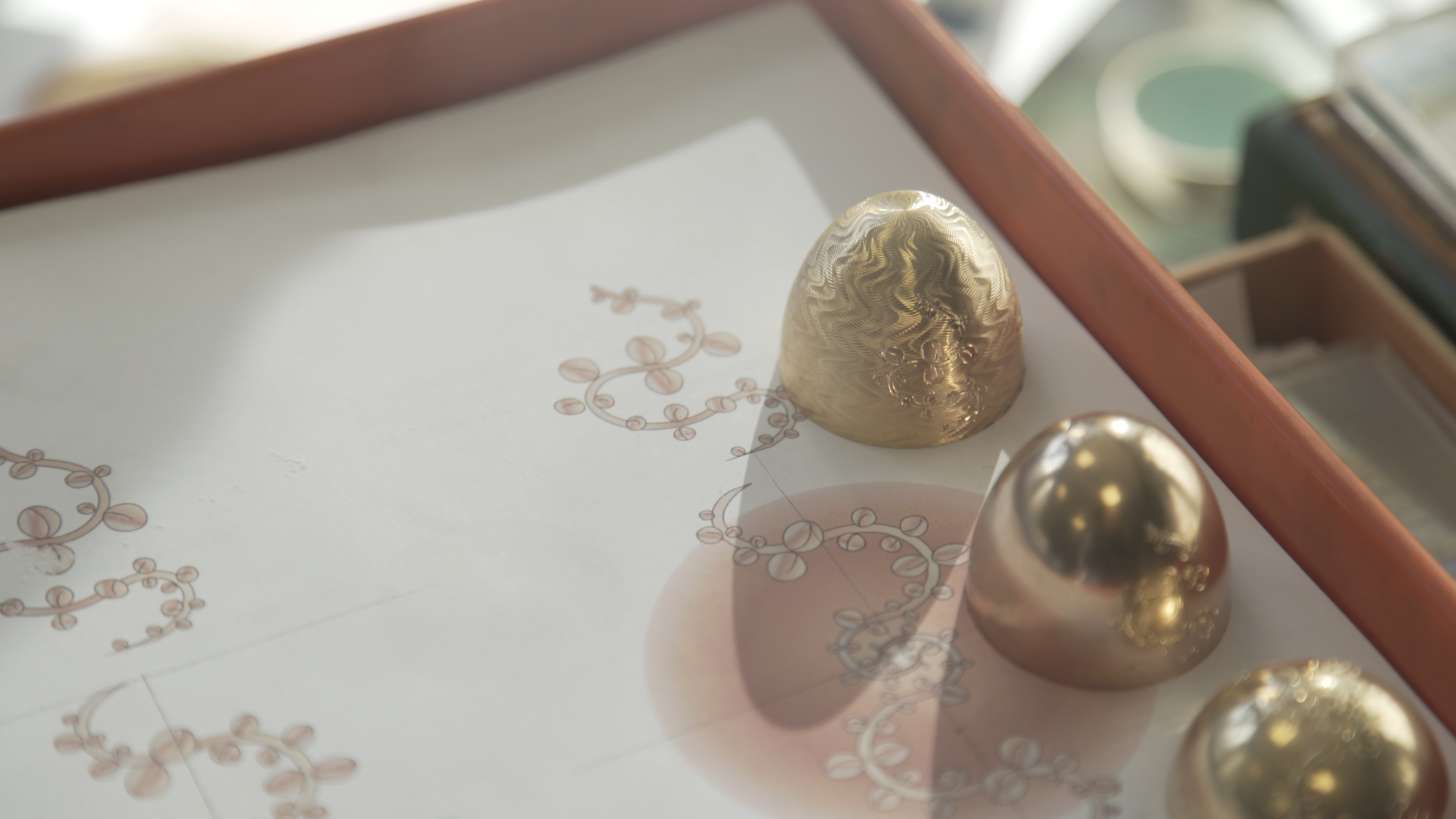 Close-up of Fabergé enamel gold egg-shaped jewellery forms displayed on top of hand-drawn design sketches, highlighting the craftsmanship and heritage-inspired design process.