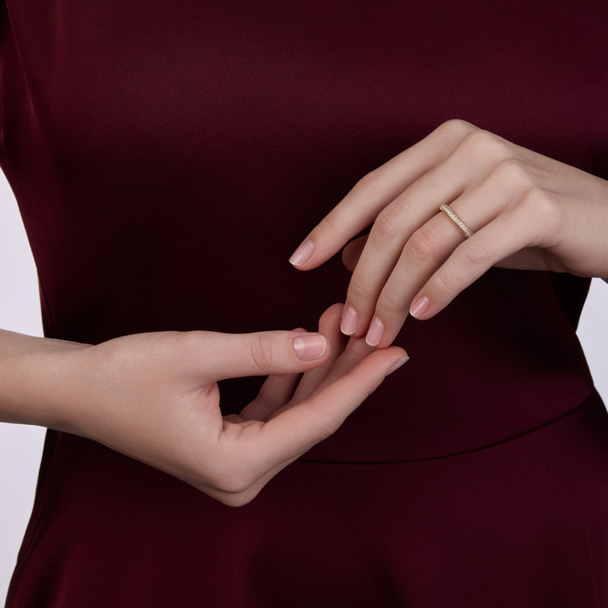 Fabergé Love Eternity Ring with Diamonds, delicate yellow gold eternity band set with pavé white diamonds, styled on the hand against a deep burgundy silk dress for an elegant, refined look.
