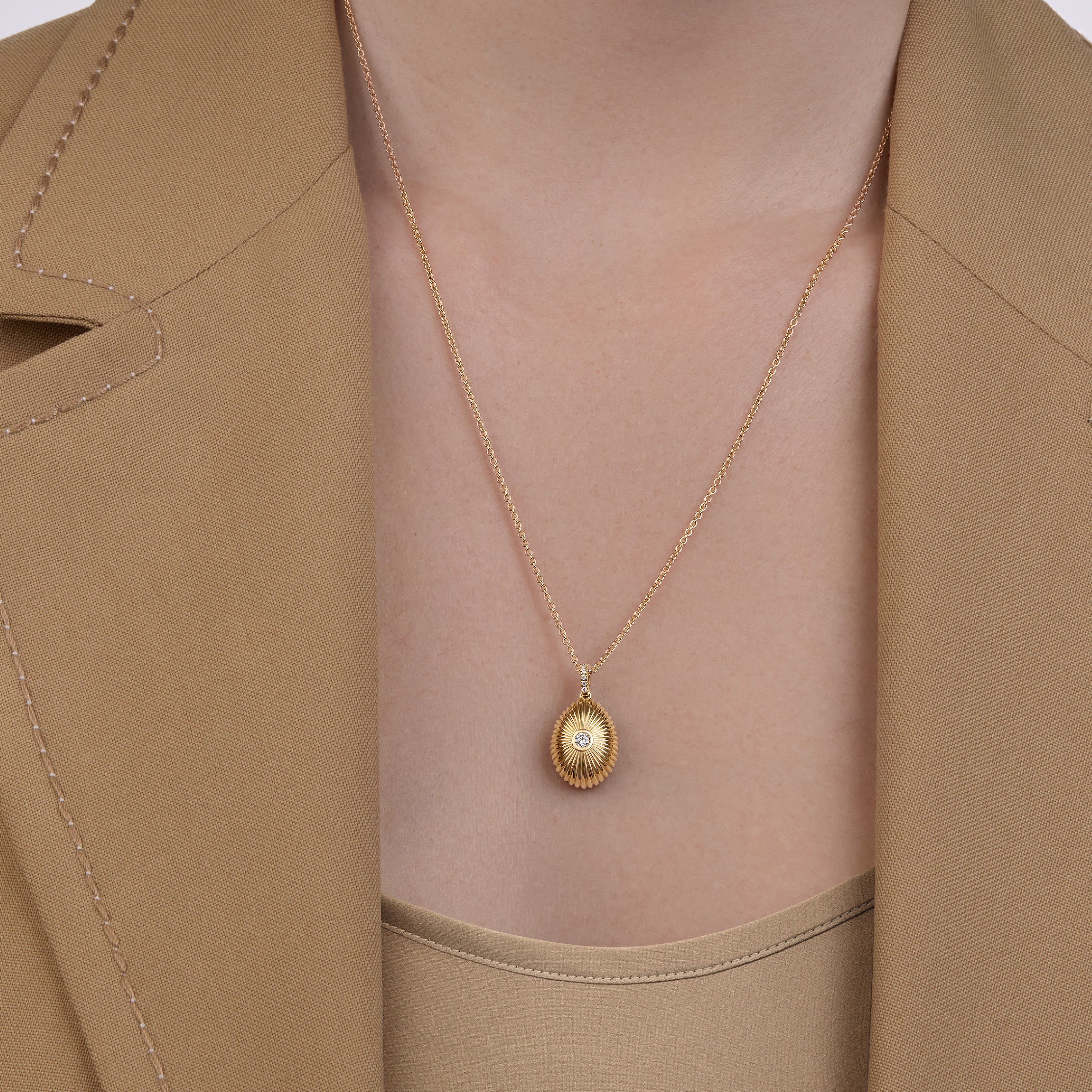 Close-up of a yellow gold Forever Mini fluted diamond pendant necklace worn with a beige blazer and matching top.