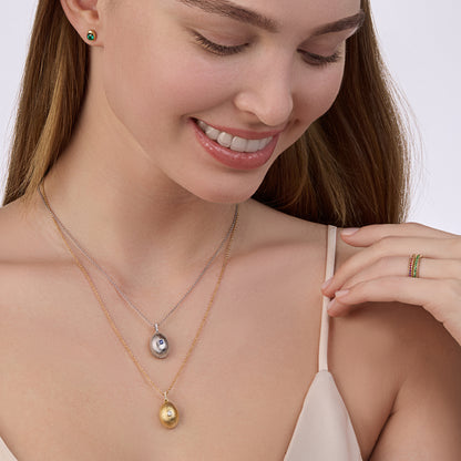 Model wearing layered yellow gold diamond and white gold sapphire fluted pendants, yellow gold love eternity rings with green and pink gemstones, and emerald code stud earrings