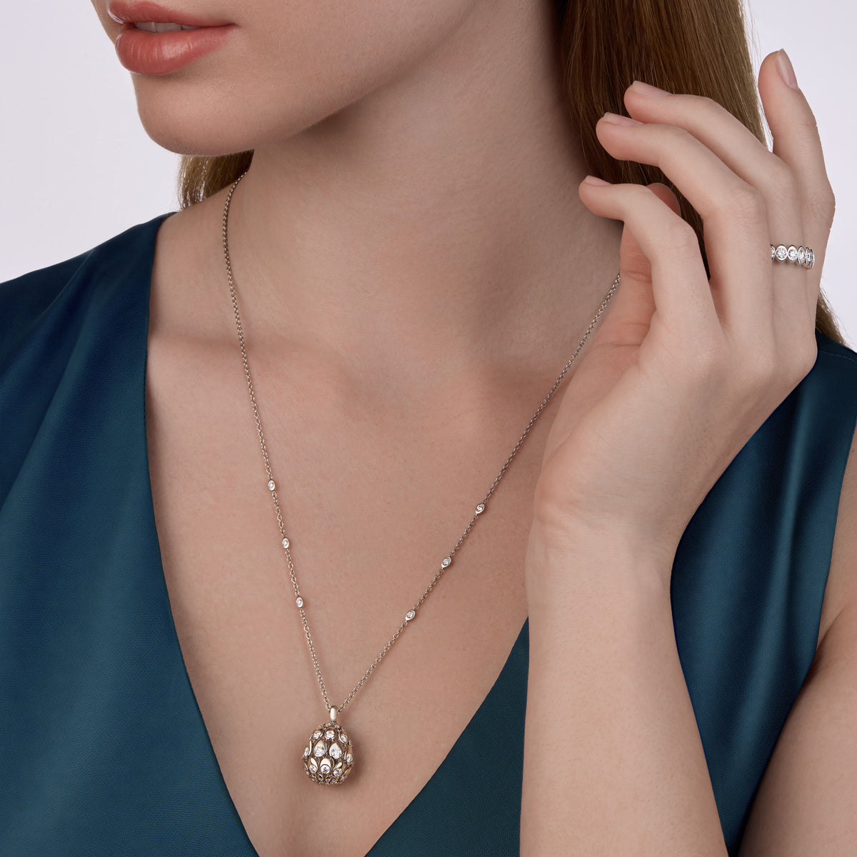 Woman wearing a white gold diamond Fabergé pendant necklace on a plain background