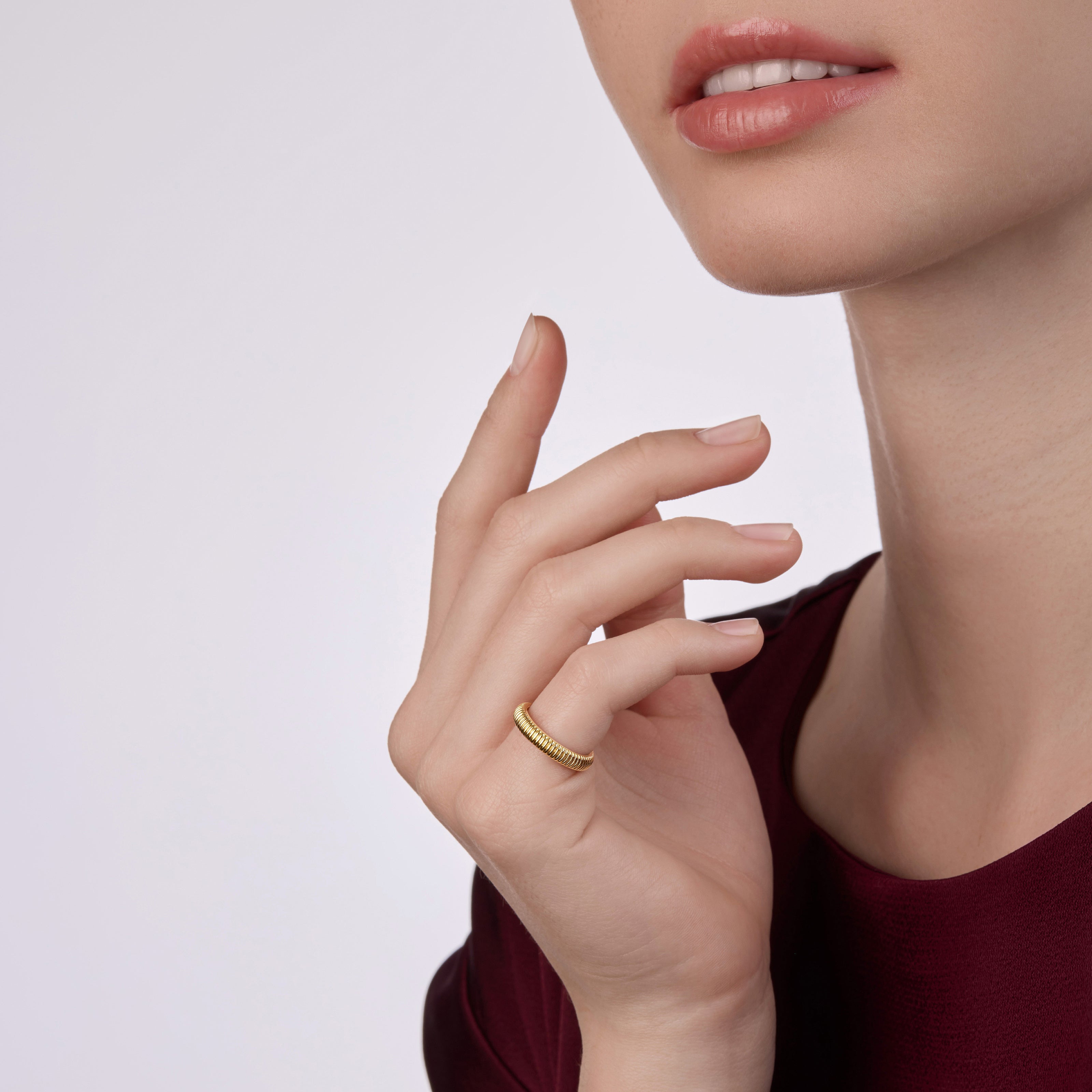Close-up of a model wearing a yellow gold fluted ring, styled with a deep burgundy dress against a soft neutral background.