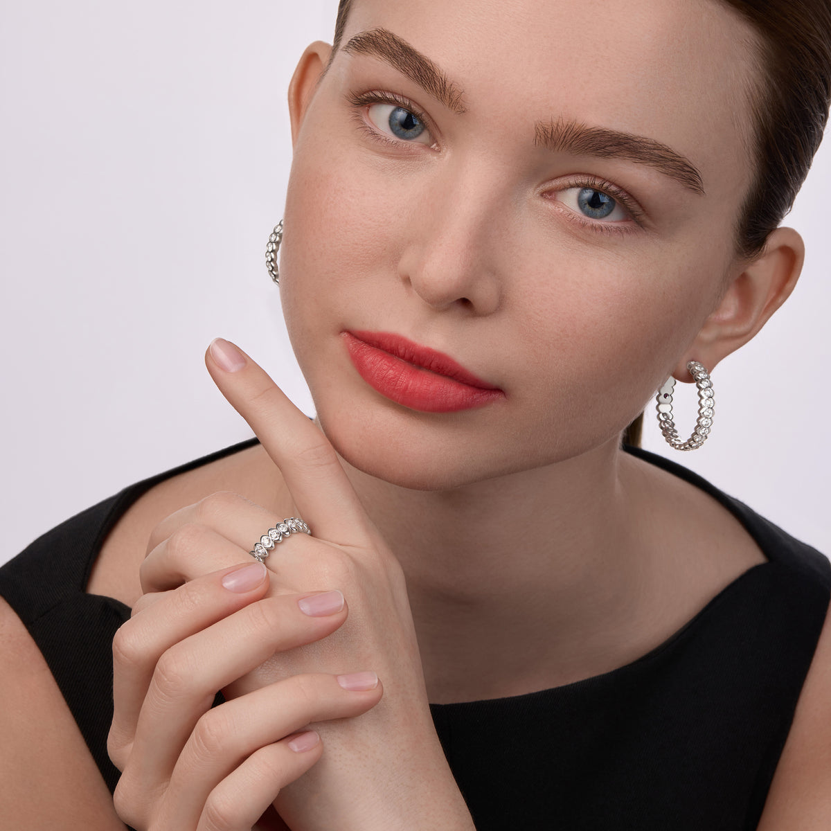 Portrait of model wearing Fabergé Code collection diamond hoop earrings and matching diamond ring in white gold with modern geometric detailing.